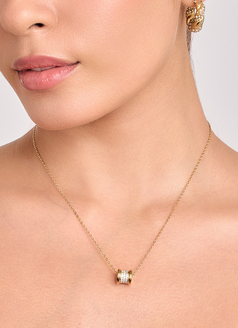 Close-up of a person wearing a gold necklace with a pendant on a neutral background